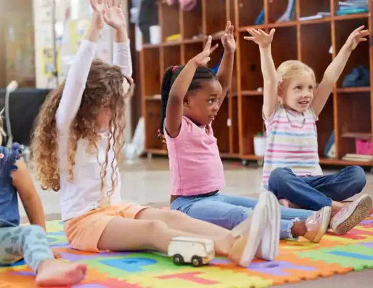Preschool children with hands raised during an activity in Discovery Park at Holt Assembly of God Kids Ministry.