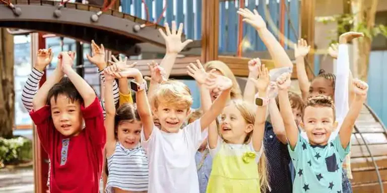 Elementary-aged children smiling with hands raised in The Adventure program at Holt Assembly of God Kids Ministry.