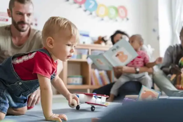 Toddler playing with a toy airplane while caregivers read to children in the Tiny Treasures nursery at Holt Assembly of God Kids Ministry.