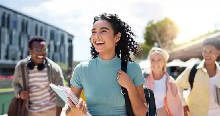 Smiling young adults walking together outdoors carrying notebooks and backpacks